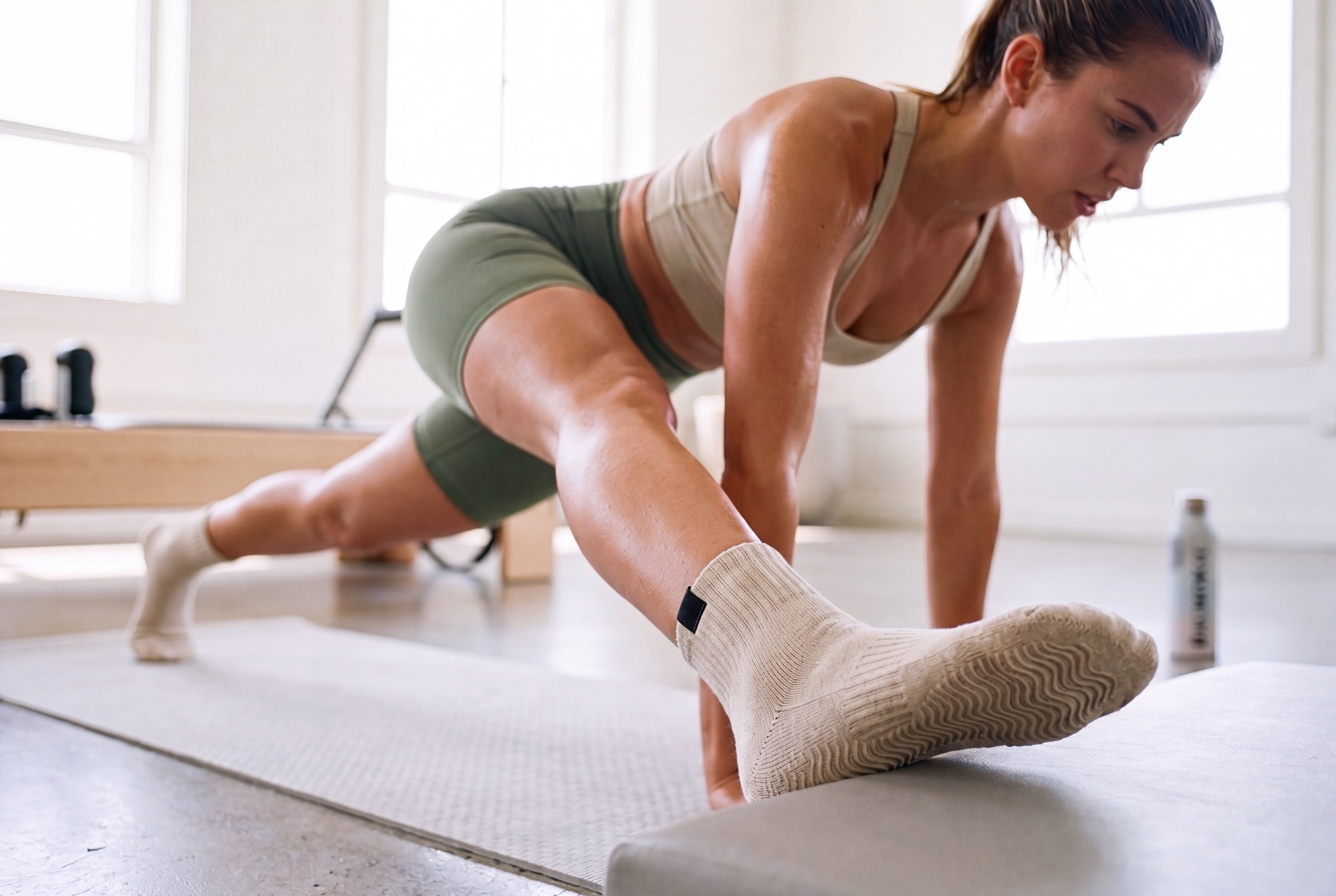 Origin — reaching forward on the reformer, Stillsole grip socks in focus.